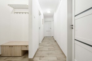 Ein schmaler Flur mit einer hölzernen Bank, weißen Wänden und einer Tür am Ende.