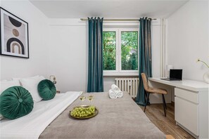 Ein Hotelzimmer mit einem Bett, einem Schreibtisch, einem Sessel, einem Heizkörper und einem fenster mit Vorhängen.