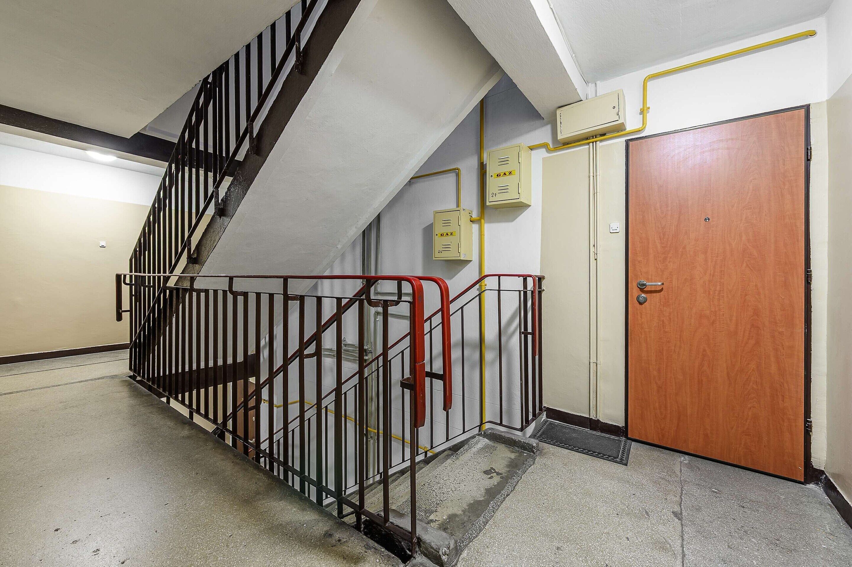 A stairwell with metal railings, a wooden door, and a fire alarm panel on the wall.