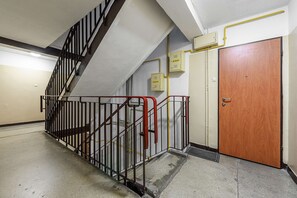 Un escalier avec des rampes en métal, une porte en bois et un panneau de déclenchement d’alarme incendie fixé au mur.