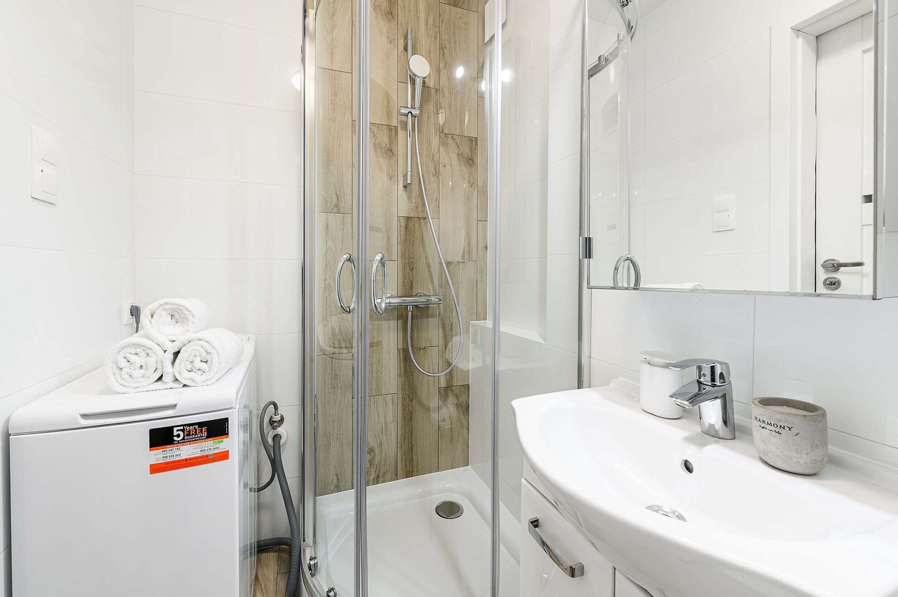 A modern bathroom with a glass shower enclosure, a white sink, and a towel rack with towels.