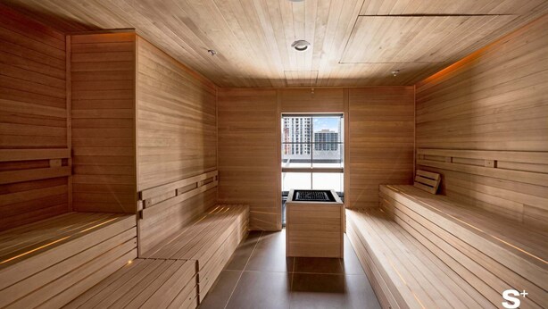 Un sauna con paredes y bancos de madera, un calentador central y vistas a edificios a través de una ventana.
