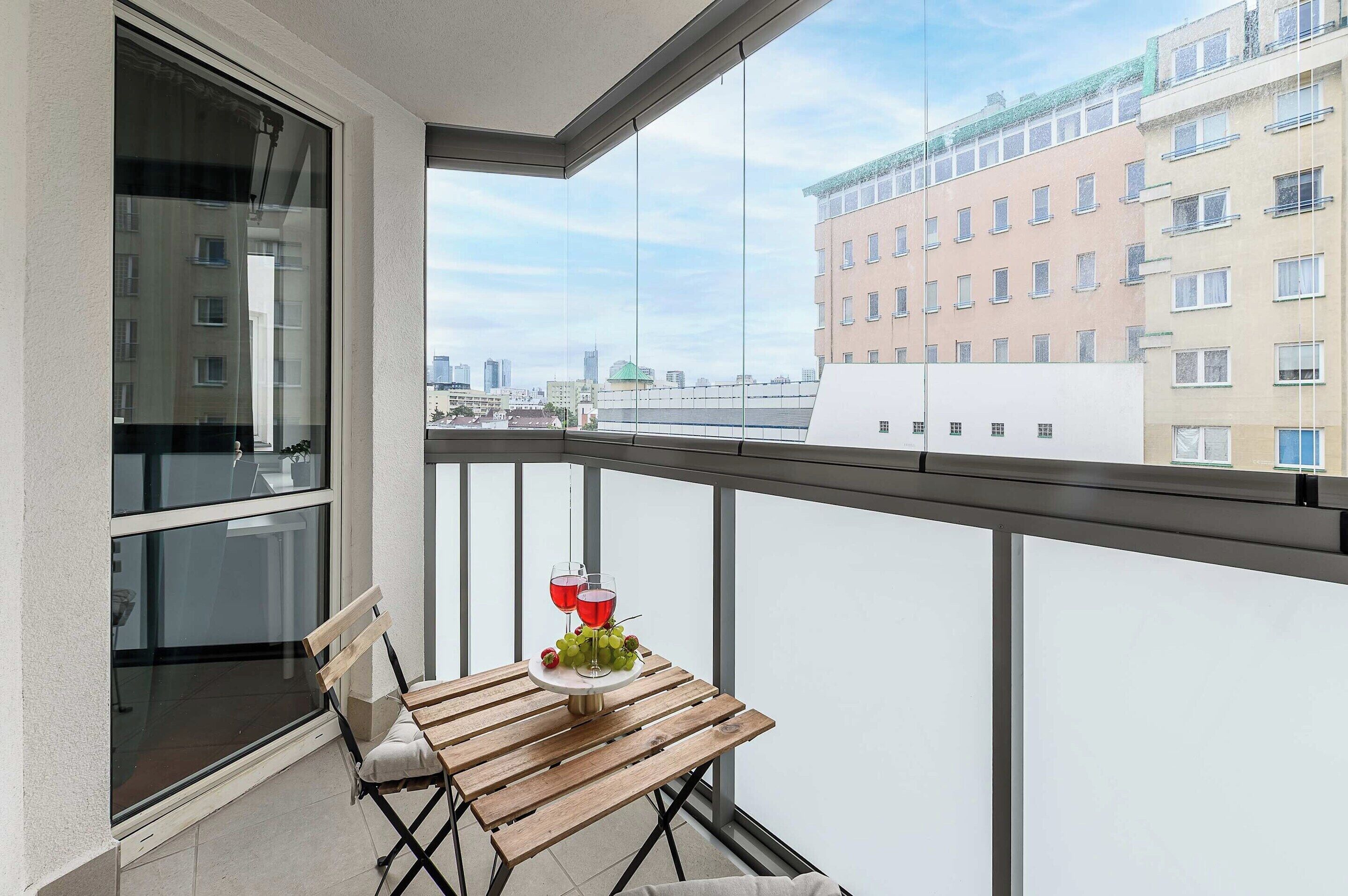 Un balcon avec une table, deux verres de vin rouge et un bouquet de raisins.