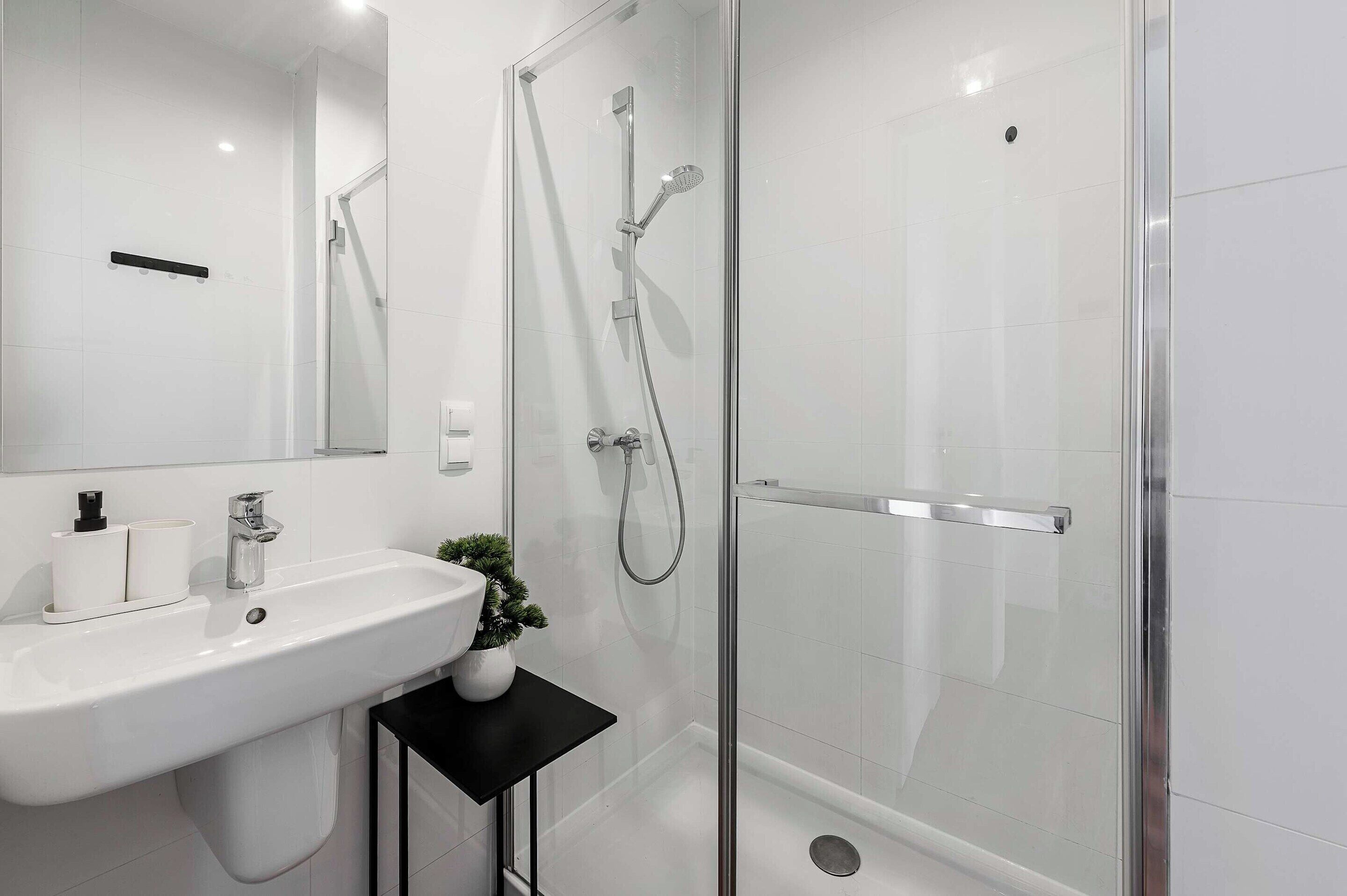 A modern bathroom with a glass-enclosed shower, a white sink with a black countertop, and a small potted plant.