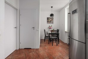 A compact kitchen with white walls, a tiled floor, a dining table with chairs, and a refrigerator. - Warsaw Stay Near Shops (Warsaw)