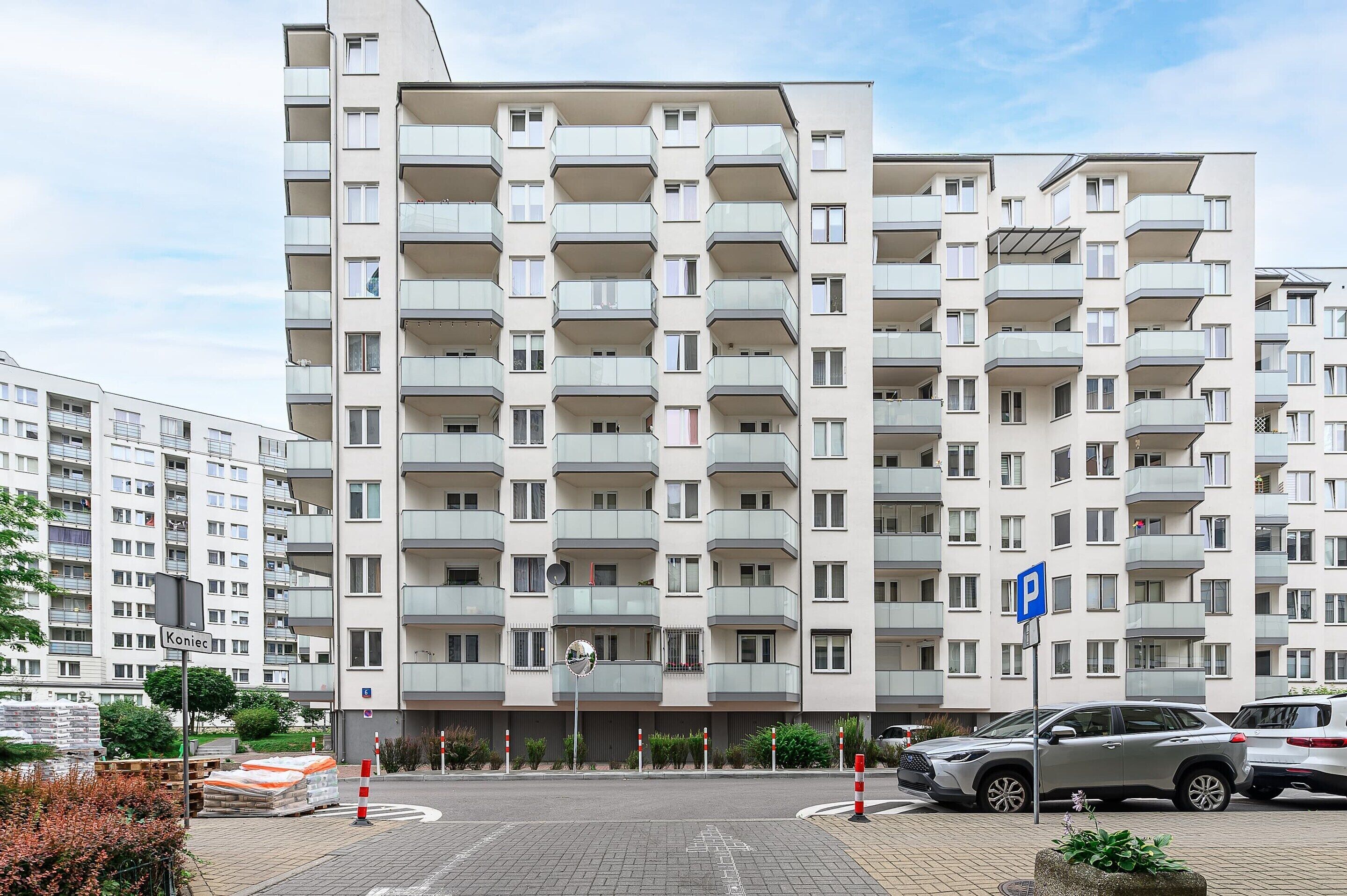 A multi-story residential building with balconies, a parking sign, and a clear sky.