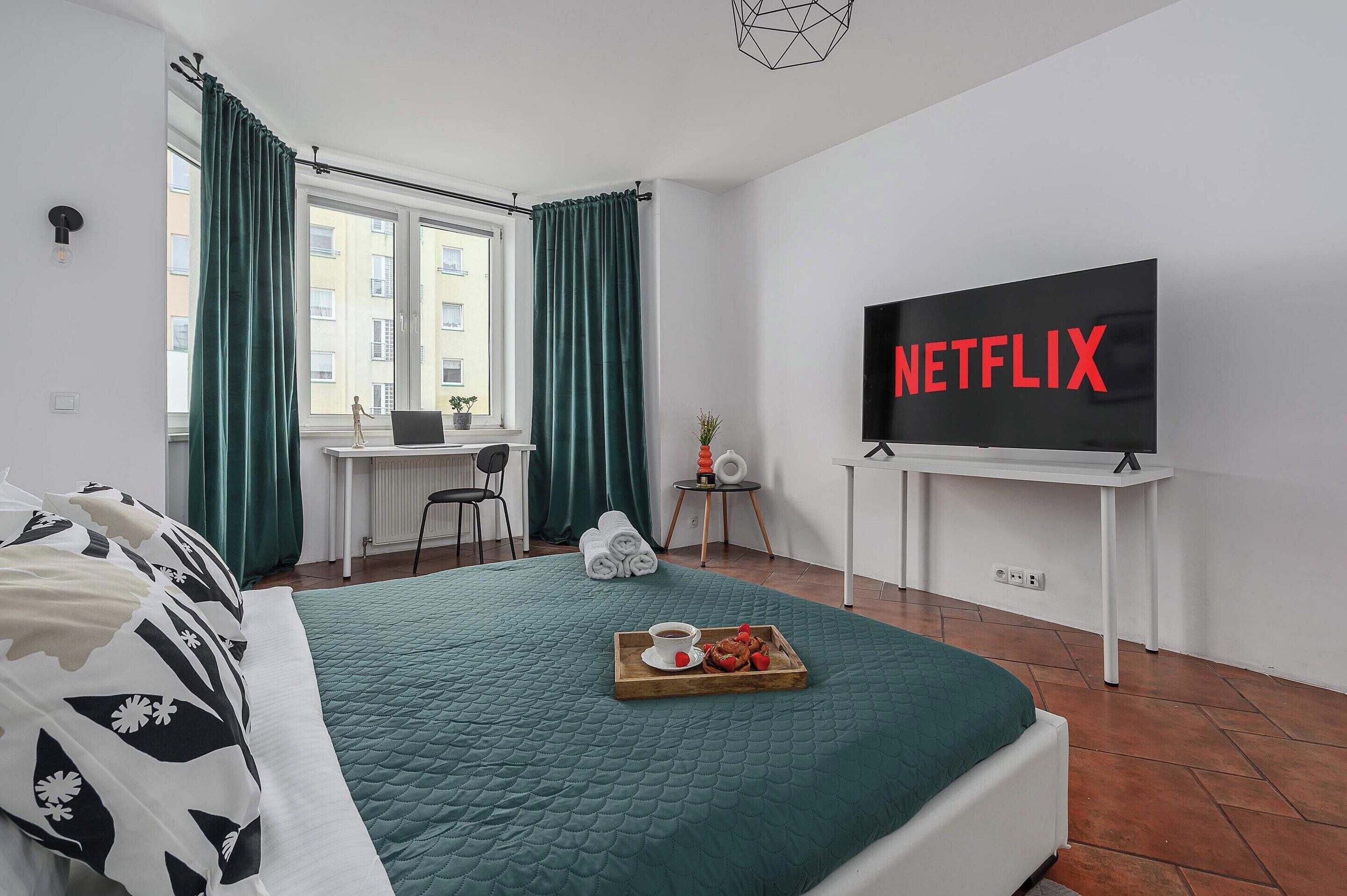 A hotel room with a bed, a desk, a TV, and a tray with food.