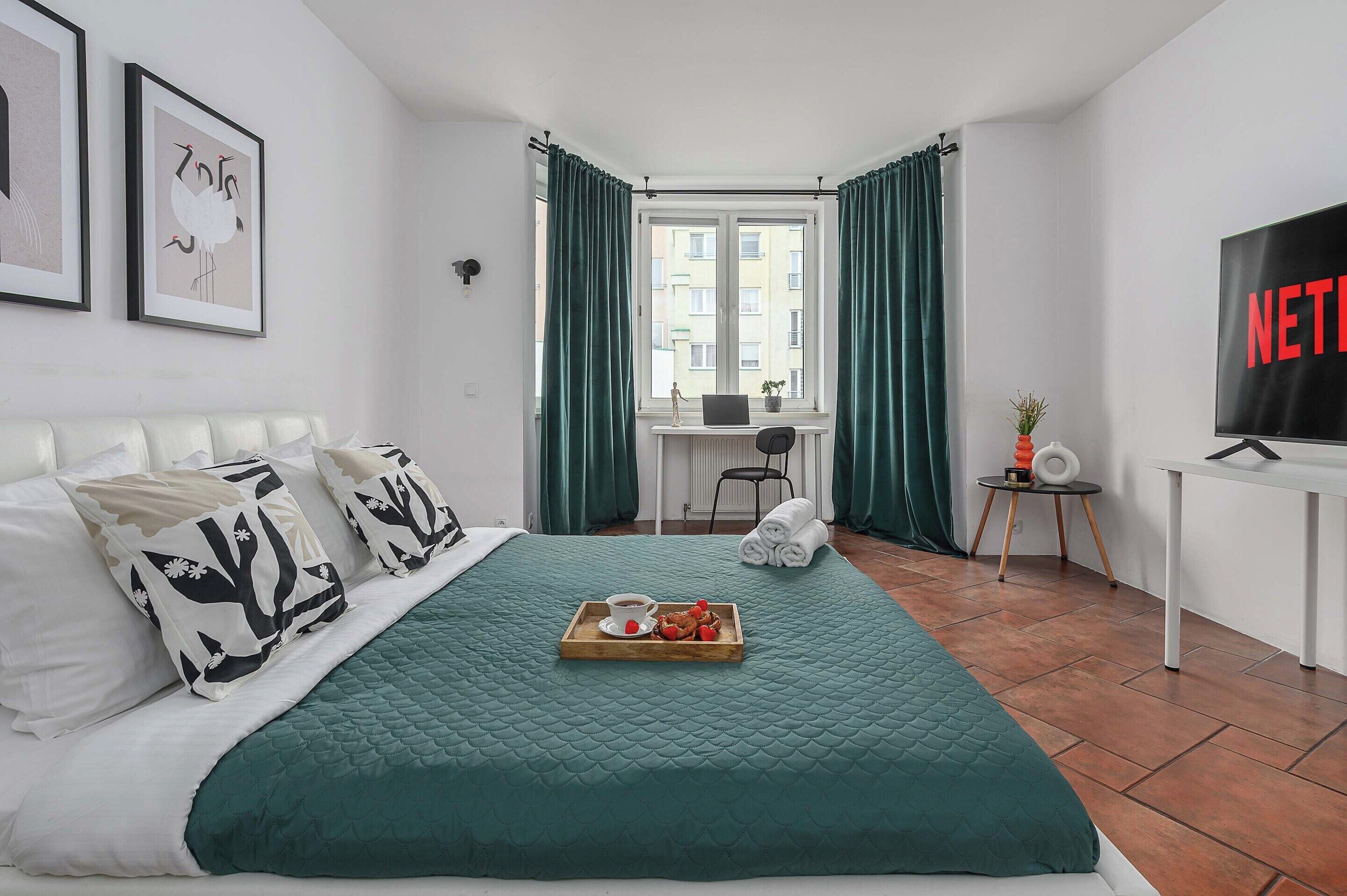A hotel room with a bed, a desk, a chair, a TV, and a window with curtains.