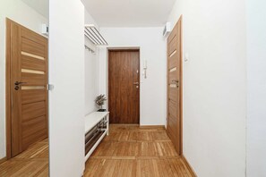 A narrow hallway with wooden flooring, a central door, and a small bench with a plant. - Stay in Warsaw Center (Warsaw)