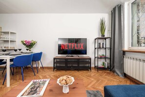 A living room with a television displaying 'NETFLIX,' a dining area with chairs and a table, and a bookshelf with books. - Stay in Warsaw Center (Warsaw)