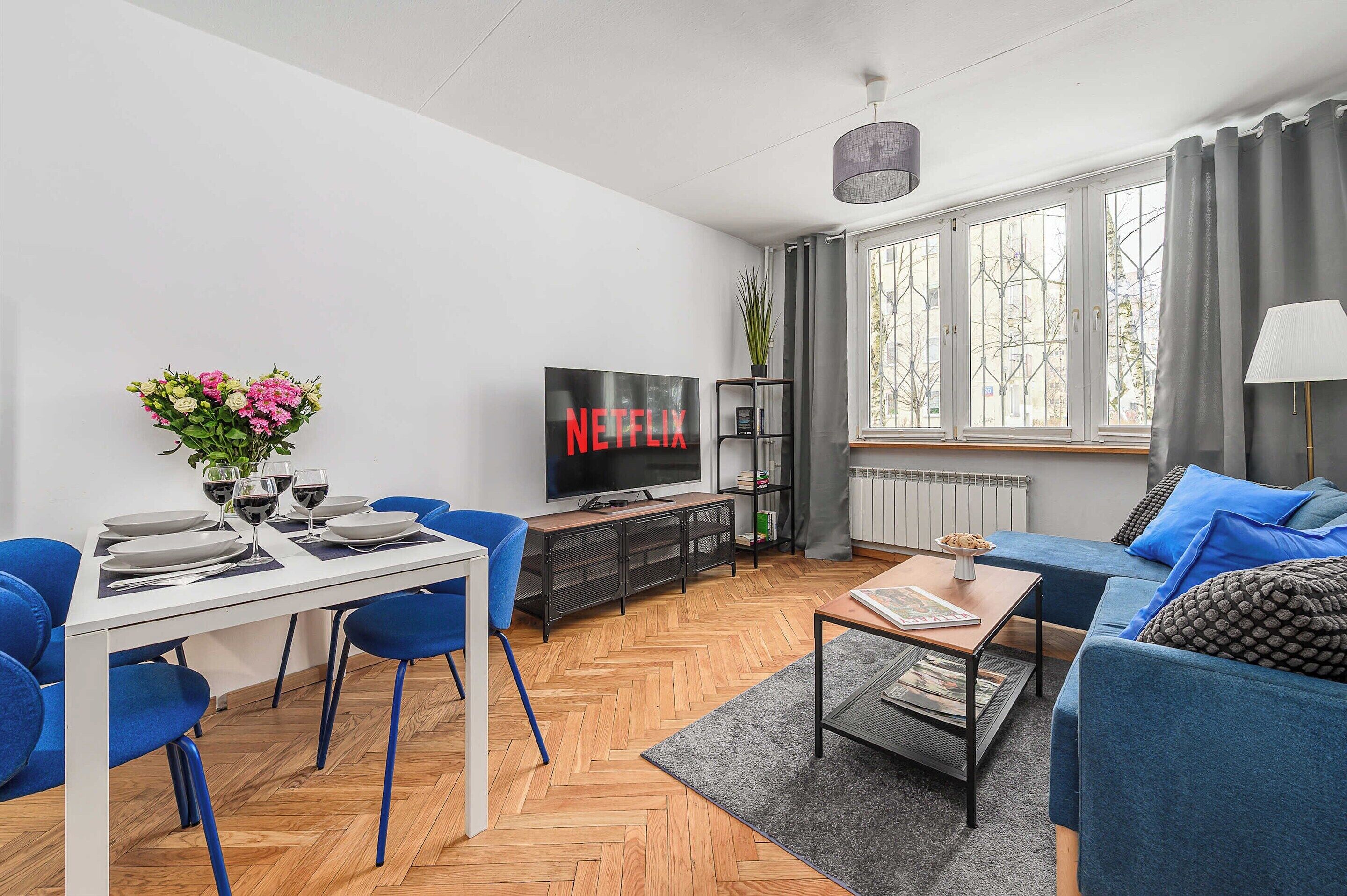Ein modernes Wohnzimmer mit Essbereich, einem Flachbildfernseher und einem großen Fenster mit Vorhängen.