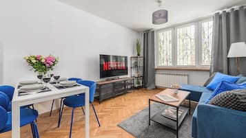 A modern living room with a dining area, a flat-screen TV, and a large window with curtains.