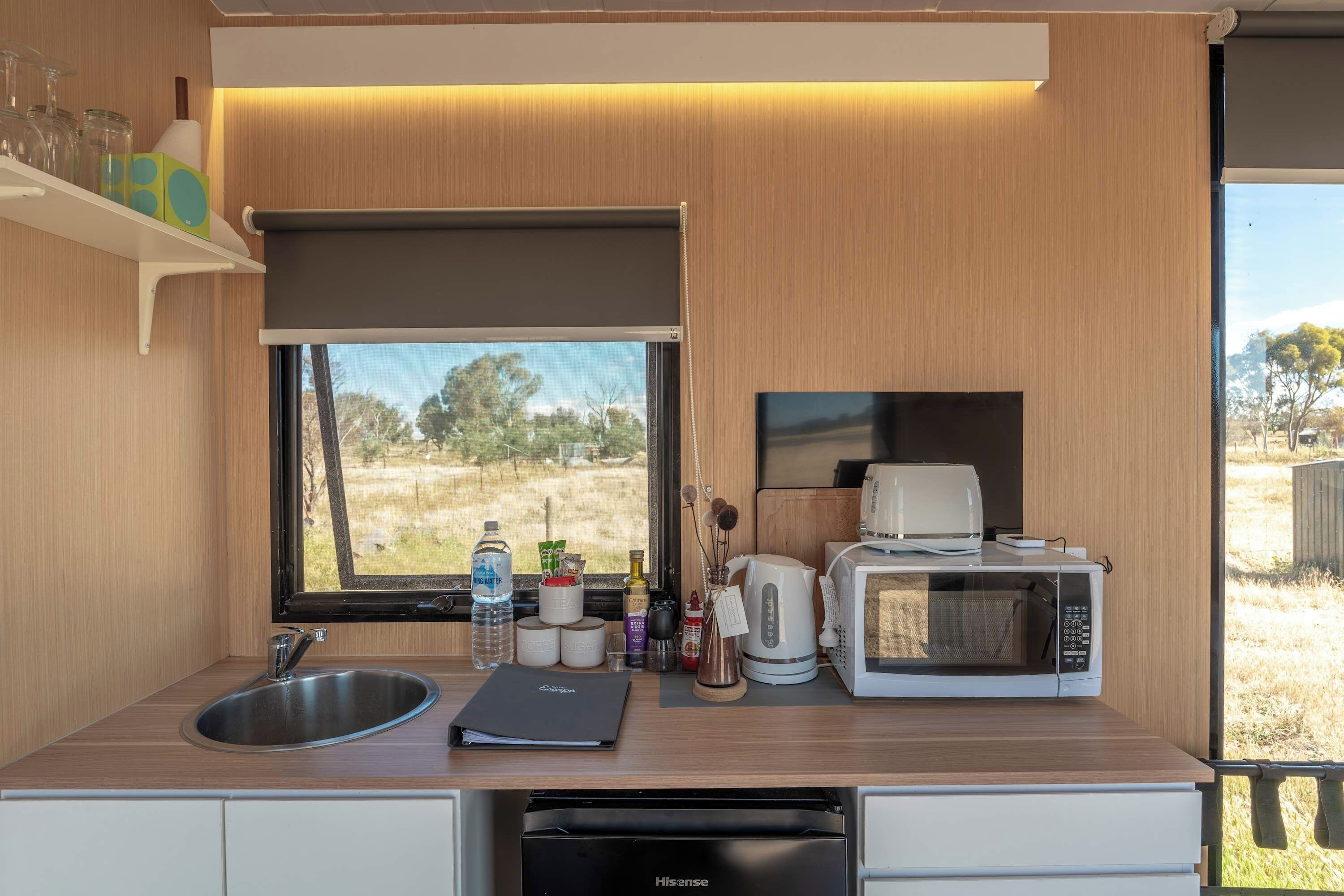 A compact kitchenette with a sink, a coffee maker, a microwave, and a view of the outdoors.