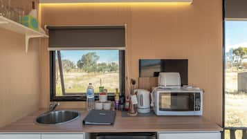A compact kitchenette with a sink, a coffee maker, a microwave, and a view of the outdoors.
