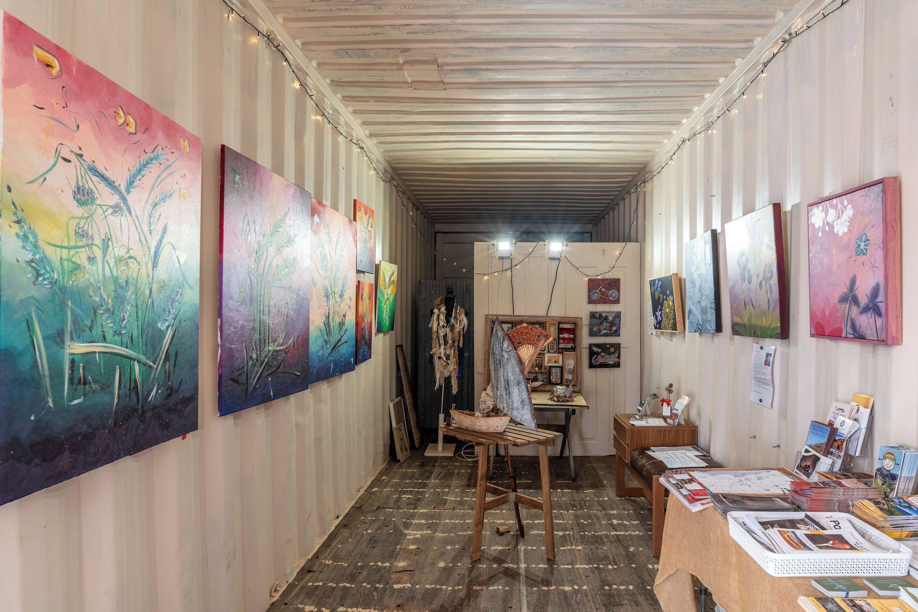 An art gallery with paintings on the walls and a wooden table with books and papers.