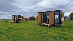 Una unidad habitacional moderna y modular con techo plano, amplias ventanas y un diseño minimalista, ubicada en un campo cubierto de césped.