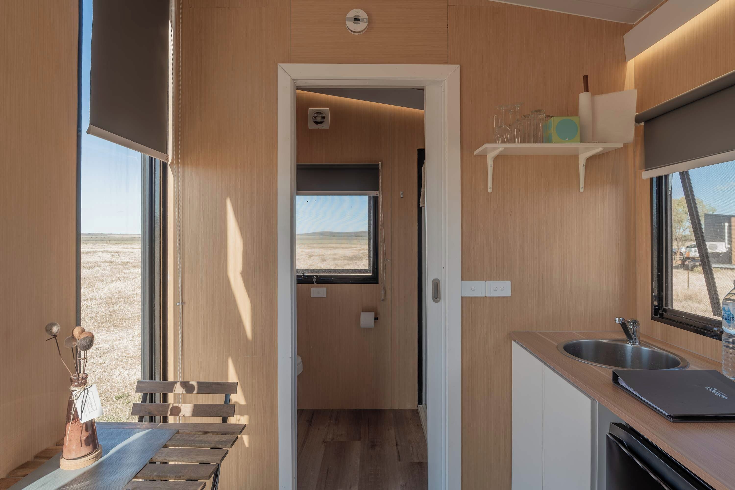 Una kitchenette compacta con un lavamanos, una pequeña encimera y una ventana con vistas a un paisaje árido.