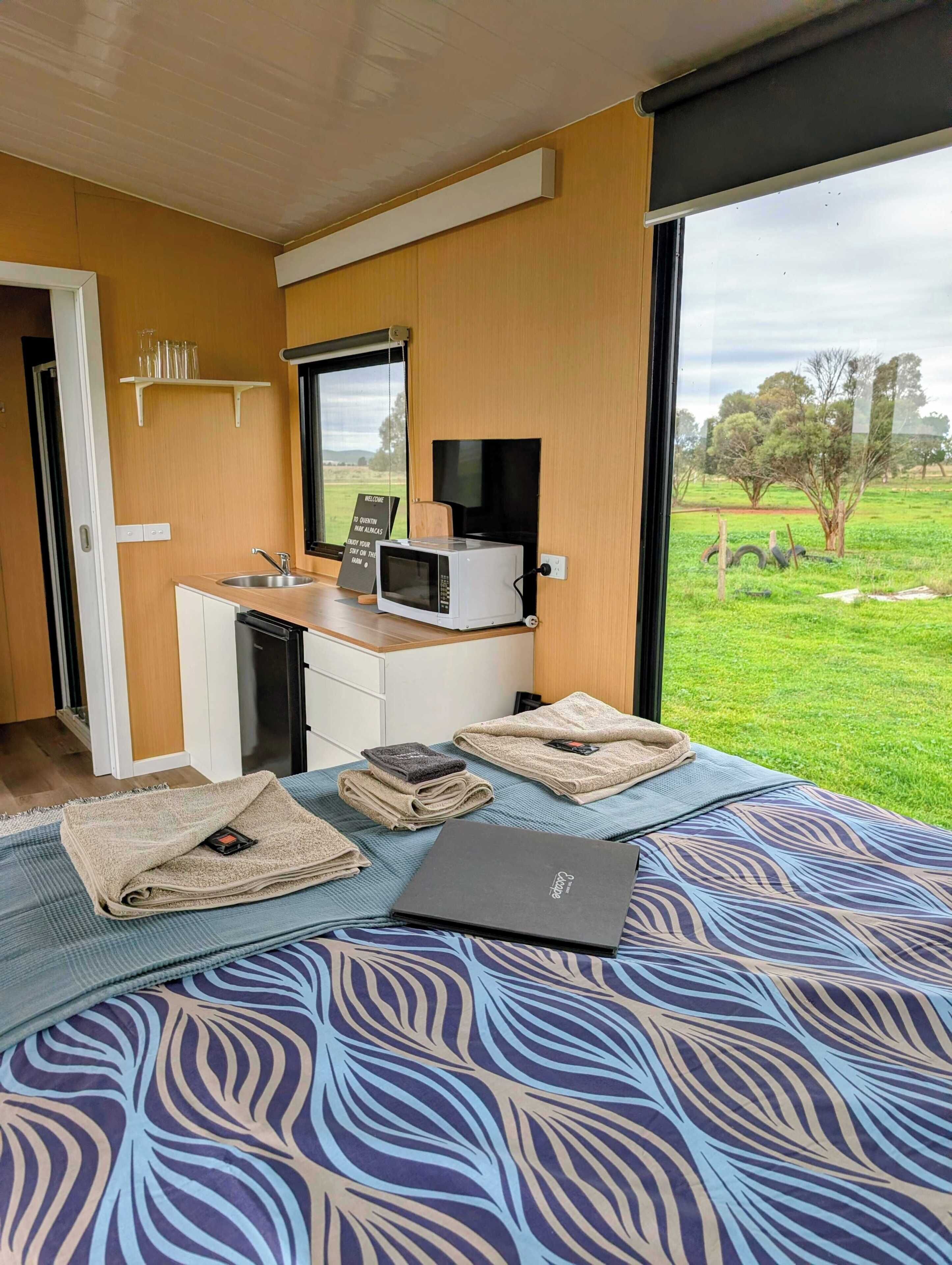 Un dormitorio con una cama, un escritorio con microondas, una computadora portátil y vistas a un paisaje verde.