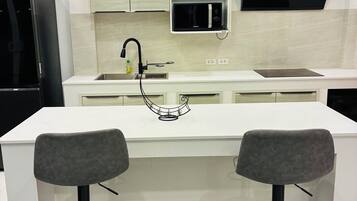 A modern kitchen with a central island, two bar stools, a built-in microwave, and a black range hood.