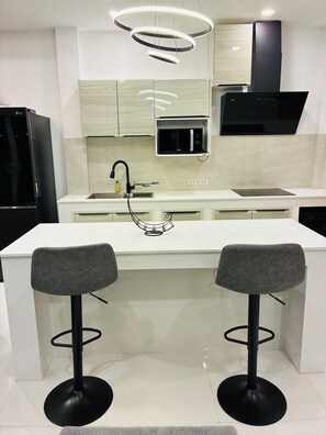 Una cocina moderna con una isla central, dos taburetes de bar, un microondas integrado y una campana extractora negra.