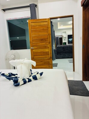 Habitación de hotel con cama, puerta de madera, ventilador y vista al área de estar.