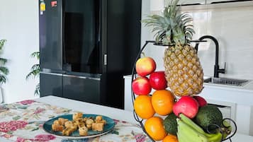 Una cocina con un refrigerador negro, una cesta de fruta en la encimera y un mantel con motivos florales.