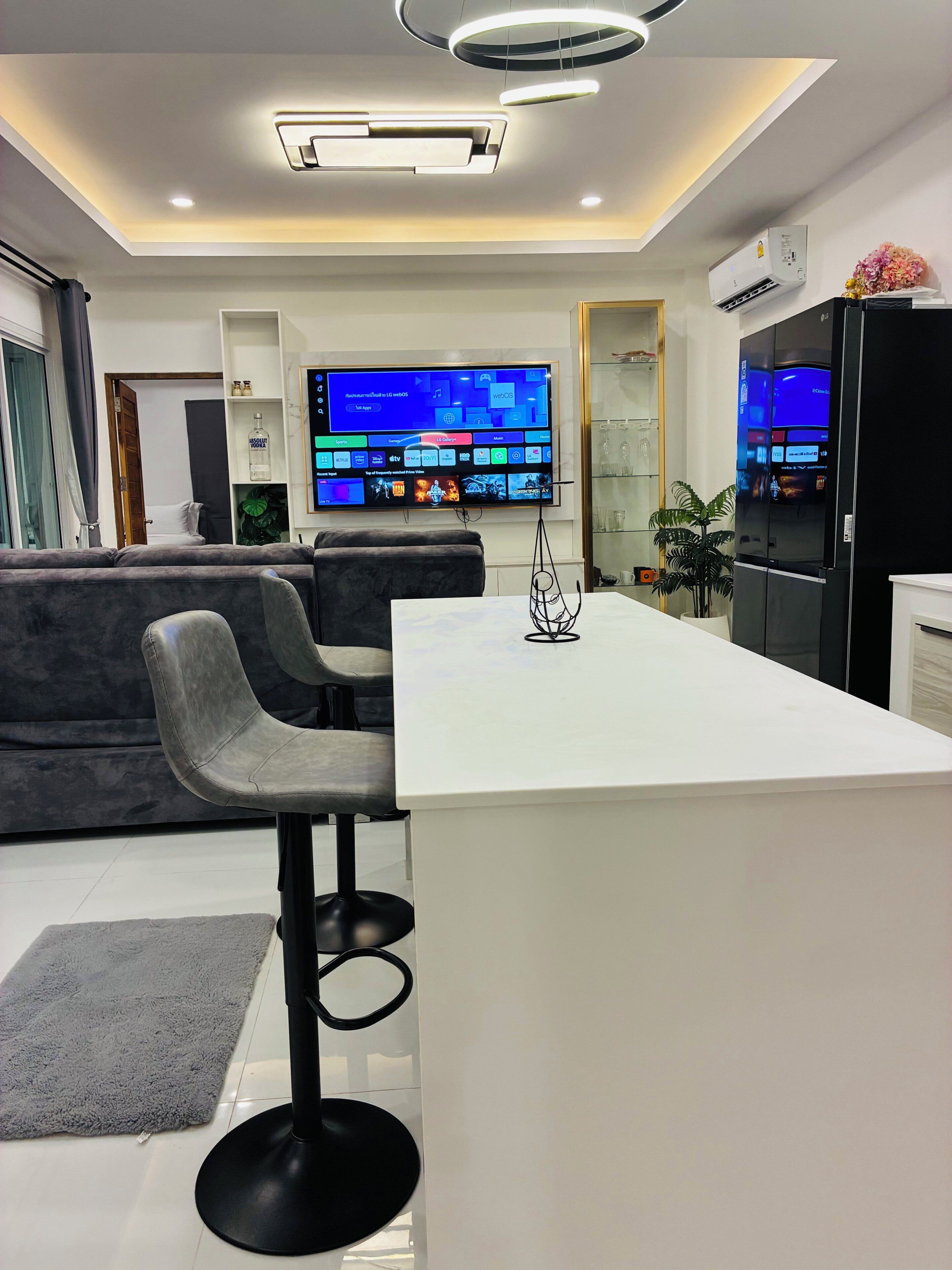 A modern kitchen with a central island, bar stools, a flat-screen TV, and built-in appliances.
