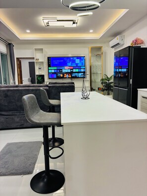 Una cocina moderna con una isla central, taburetes de bar, televisor de pantalla plana y electrodomésticos integrados.
