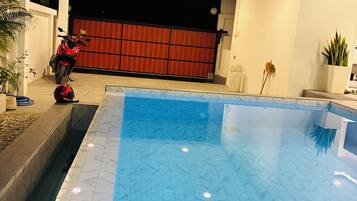 A swimming pool with a tiled floor, a red motorcycle parked outside, and a red gate.