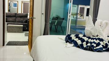 A hotel room with a bed, a view of the swimming pool, and a dining area.