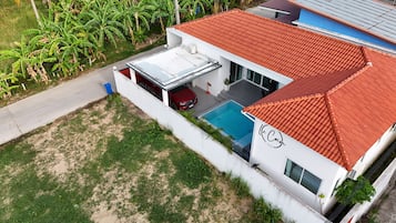 A modern villa with a swimming pool, a red car, and a red-tiled roof.