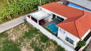 Una villa moderna con piscina, un coche rojo y techo de tejas rojas.
