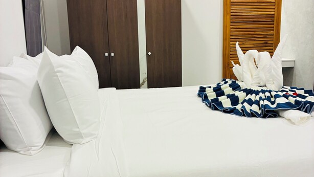Habitación de hotel con cama, almohadas blancas, manta estampada en azul y blanco, y un armario de madera.