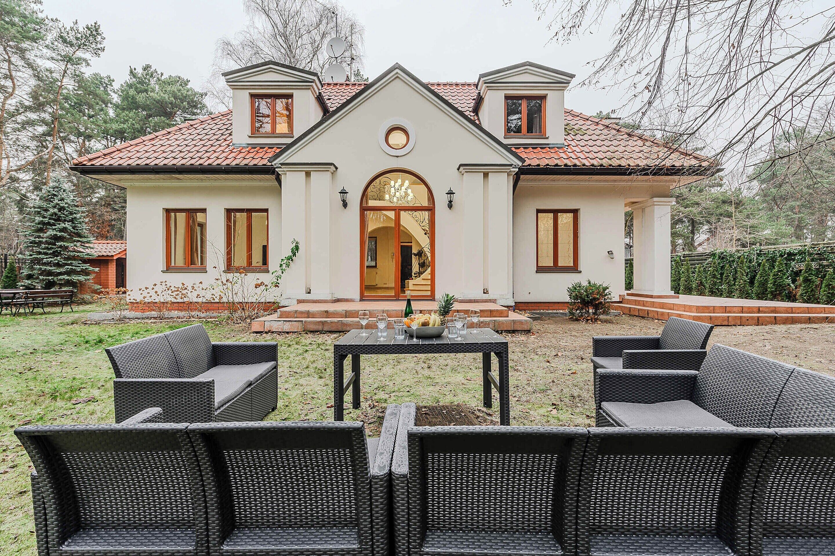 A two-story house with a symmetrical facade, a central entrance with a decorative arch, and a small porch area with wicker furniture.