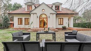 A two-story house with a symmetrical facade, a central entrance with a decorative arch, and a small porch area with wicker furniture.