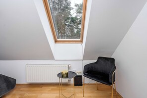 A small room with a sloped ceiling, a skylight, a radiator, a table with a decorative item, and a black chair.