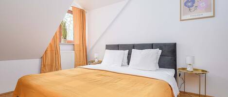 A bedroom with a bed, a nightstand, a lamp, a window with curtains, and a framed picture on the wall.