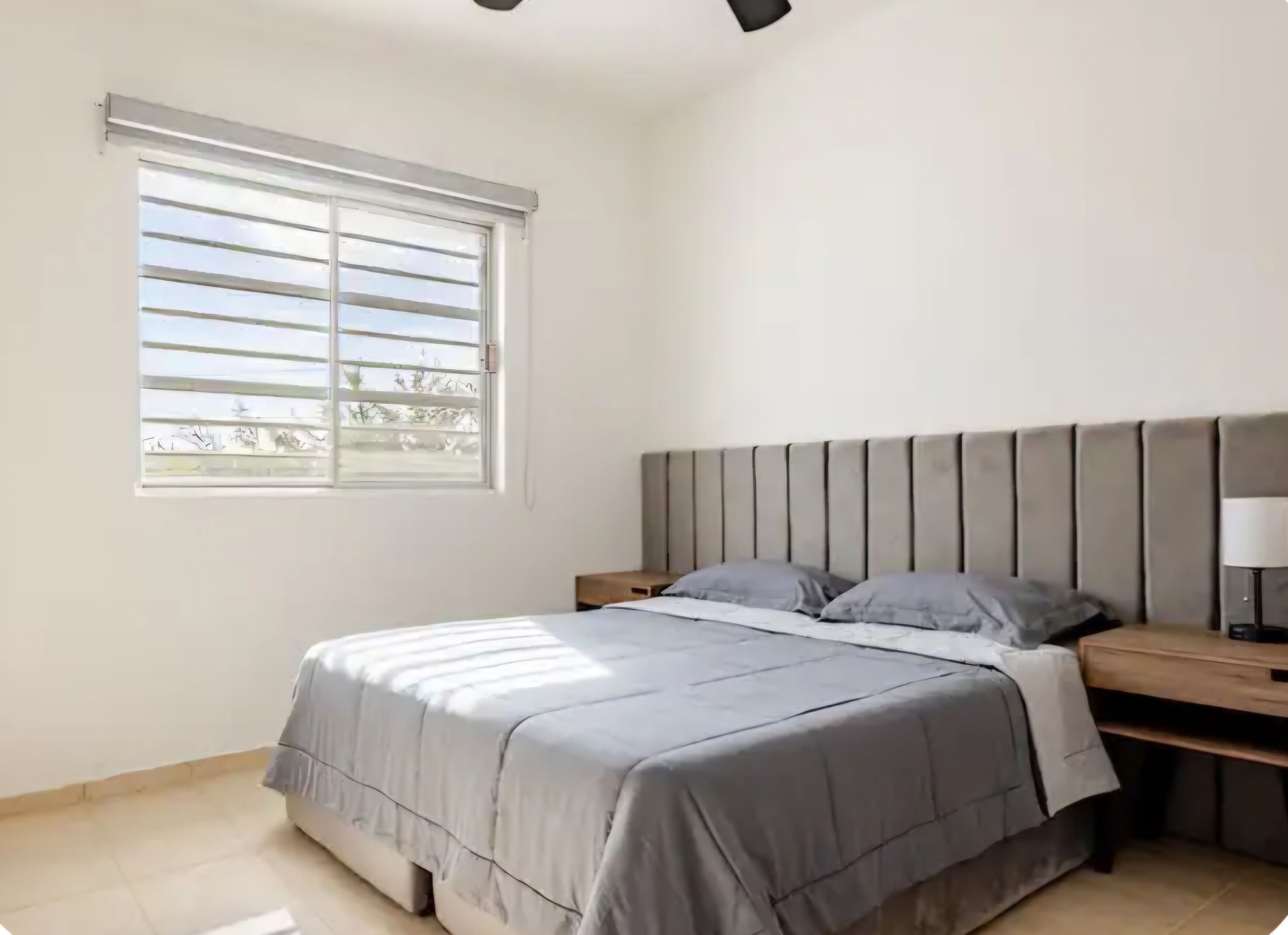 A bedroom with a bed, a nightstand, a window, and a ceiling light fixture.