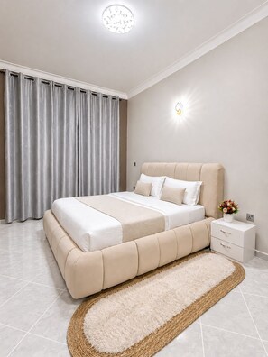 Un dormitorio con cama, mesita de noche, luz empotrada en la pared y ventana con cortinas.
