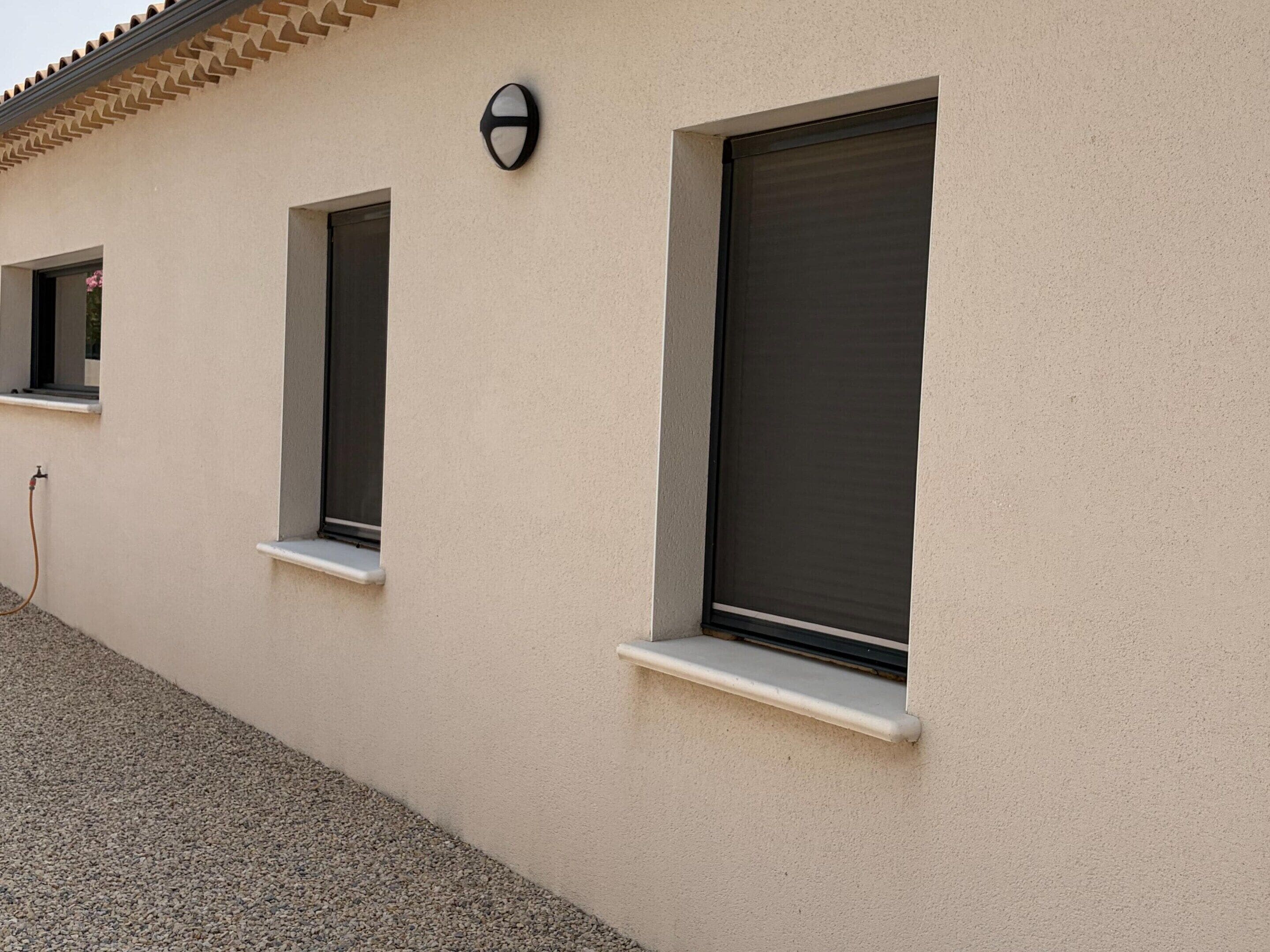 Fachada de edifício com três janelas, cada uma com peitoril branco e veneziana escura.