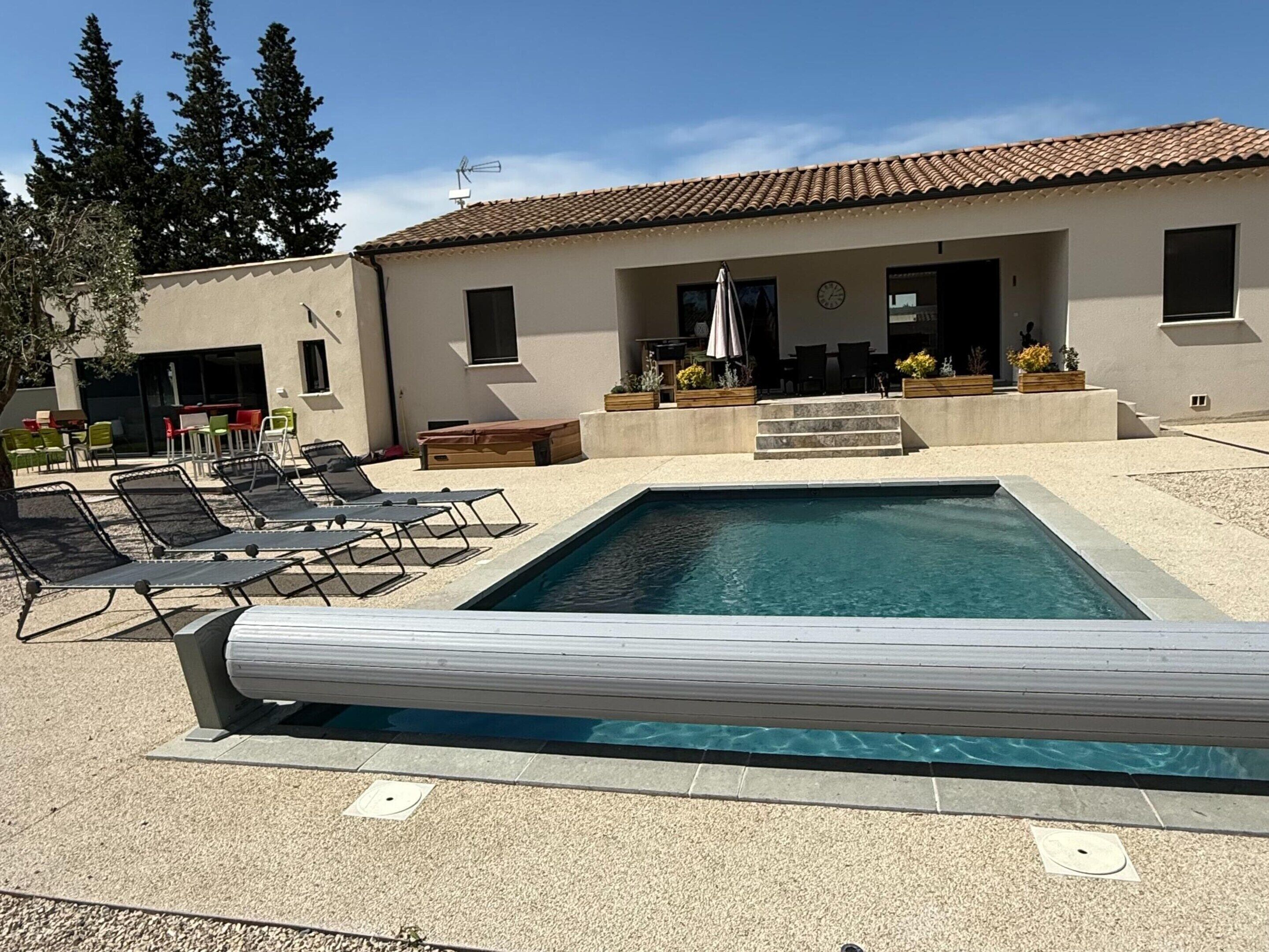 A swimming pool with lounge chairs, a covered patio area, and a building with a tiled roof.