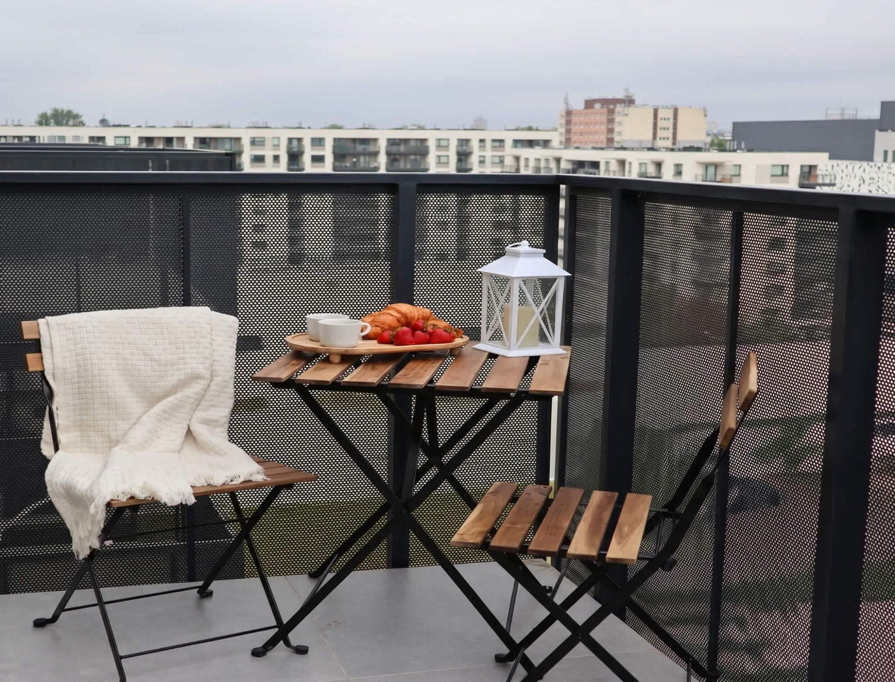 Un balcon avec une table dressée pour deux personnes, une chaise blanche et une lanterne blanche.