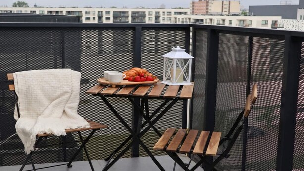 Un balcón con una mesa dispuesta para dos, una silla blanca y un farol blanco.
