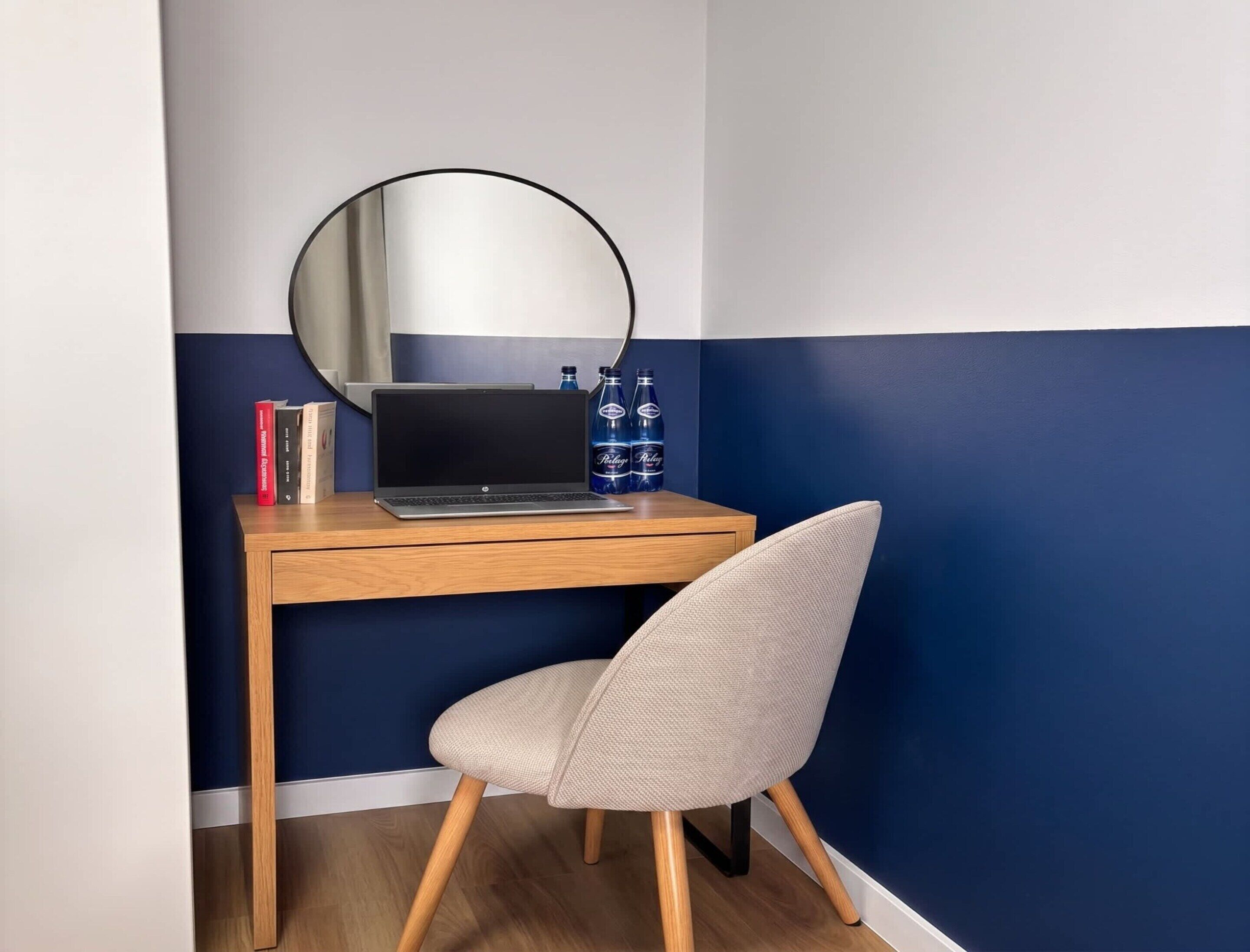 A corner desk with a laptop, a mirror, and two bottles of water.
