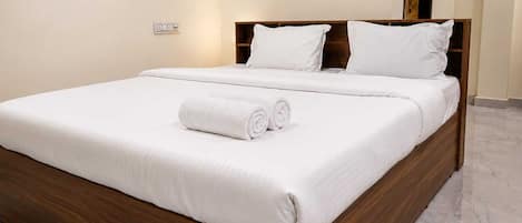 A neatly made bed with white linens and a rolled towel, a wooden headboard, and a marble floor.