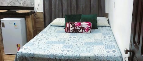 Un dormitorio con cama, un refrigerador pequeño, aire acondicionado de pared y una cortina.