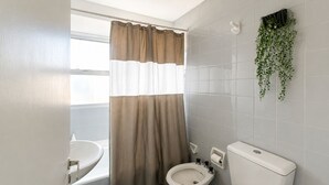 Baño con inodoro, bidé, lavamanos y una ventana con cortina.