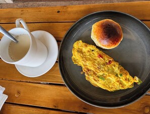 A breakfast setting with a plate of food, a cup of coffee, and a bread roll on a wooden table.