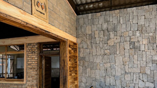 Un espacio interior con una pared de piedra, una mesa de madera con sillas y un cartel sobre la puerta.