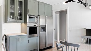 A modern kitchen with grey cabinets, a built-in microwave, a refrigerator, and a dining area with a bench.